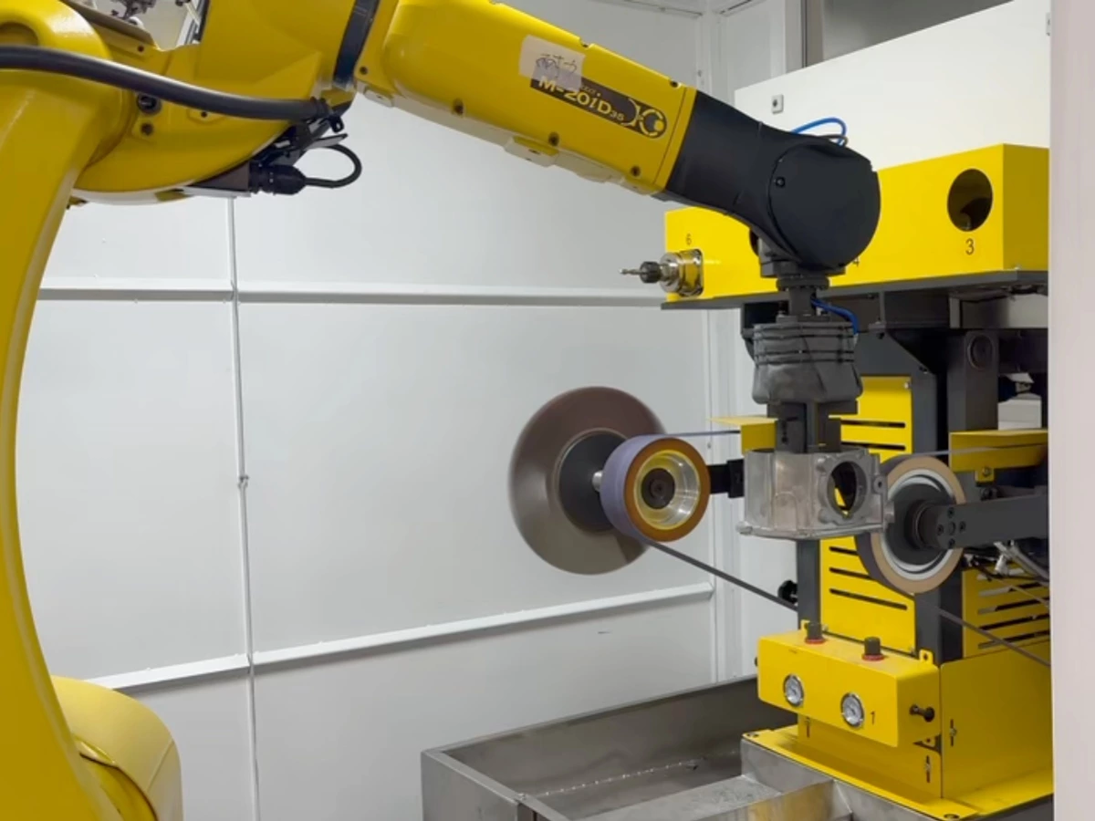 Robot-held aluminum casting contacting an abrasive belt for edge deburring