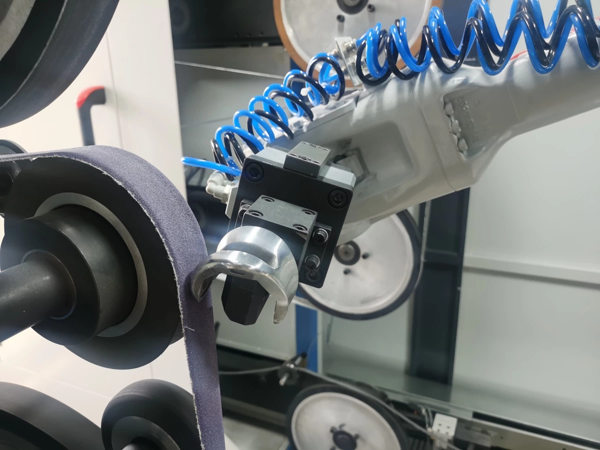 Robot holding a metal workpiece against an abrasive belt